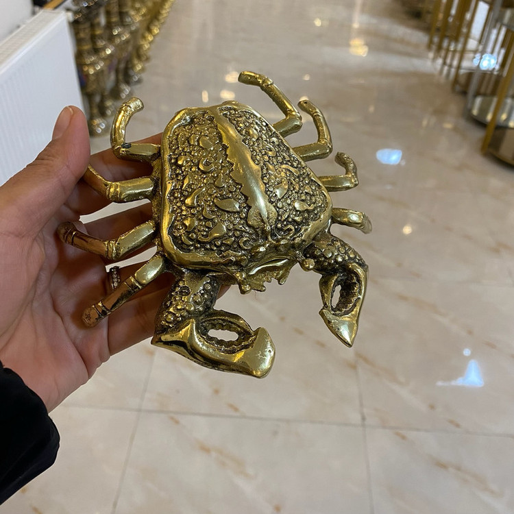 جاسیگاری طرح خرچنگ برنجی طلایی لوکس با درب لولایی بازشونده، جزییات ظریف چنگالها و بدنه، محفظه خاکستر عمیق و صقلکاری زرین متالوکس بر روی میز
