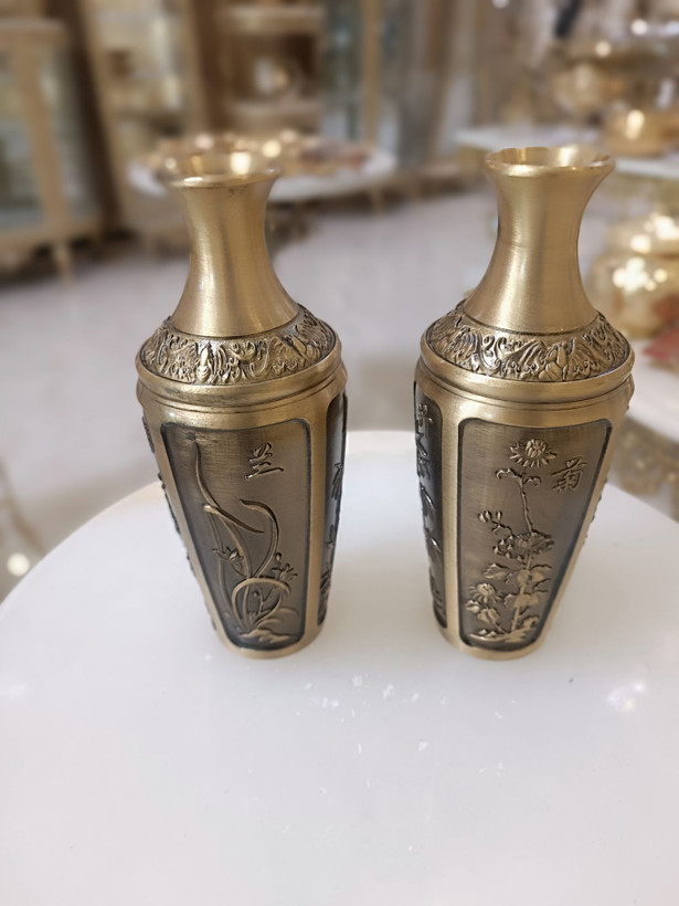 دو عدد گلدان برنجی با رنگ آنتیک و حکاکیهای ظریف طرح گل و گیاه روی میز سفید فروشگاه متالوکس
