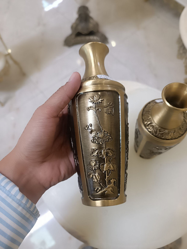 دو عدد گلدان برنجی با رنگ آنتیک و حکاکیهای ظریف طرح گل و گیاه روی میز سفید فروشگاه متالوکس